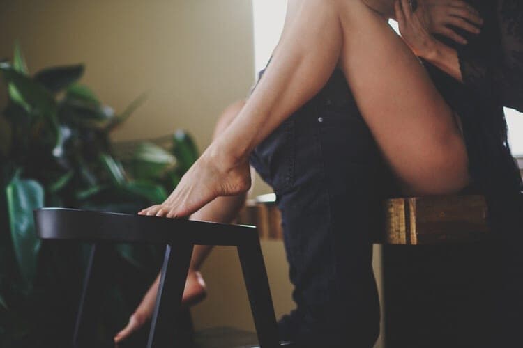 Close-up of a couple embracing on a wooden stool beside a houseplant in soft window light