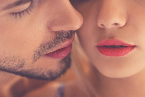 Extreme close-up of a bearded man's face beside a woman with red lipstick, their lips nearly touching