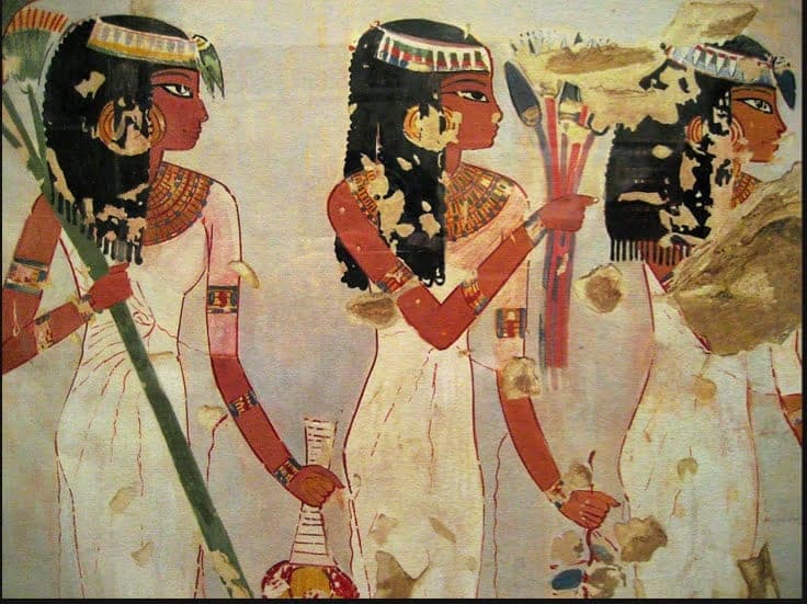 Weathered ancient Egyptian tomb painting showing three women in white dresses with elaborate black wigs and gold jewelry