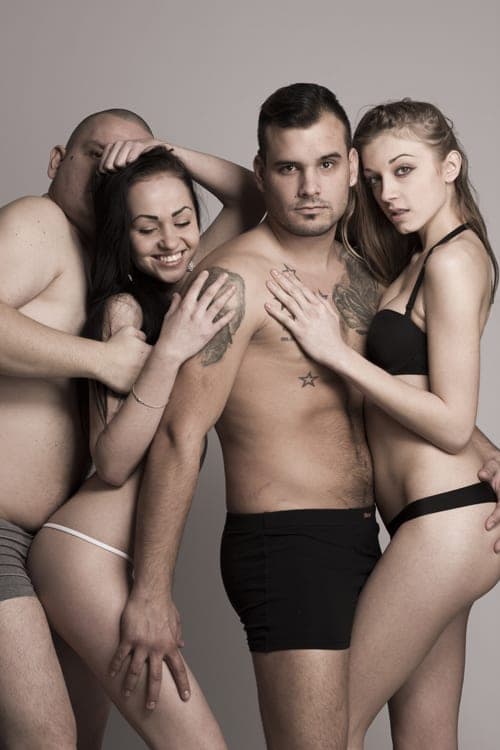 Studio portrait of two men in underwear and two women in lingerie posed closely together against a grey backdrop