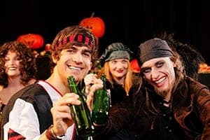 Two young men in pirate costumes and bandanas toasting green beer bottles at a Halloween party with pumpkins