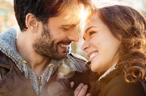 Bearded man and brunette woman in leather jackets smiling at each other in warm backlit outdoor light