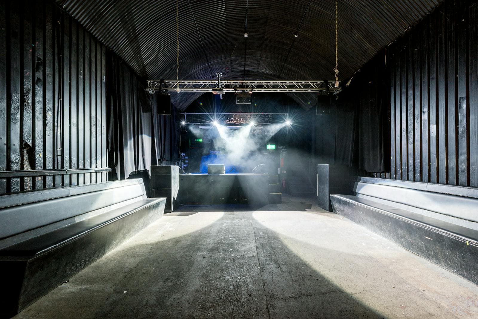 Empty nightclub interior with industrial design, stage lighting, and rows of seating awaiting guests
