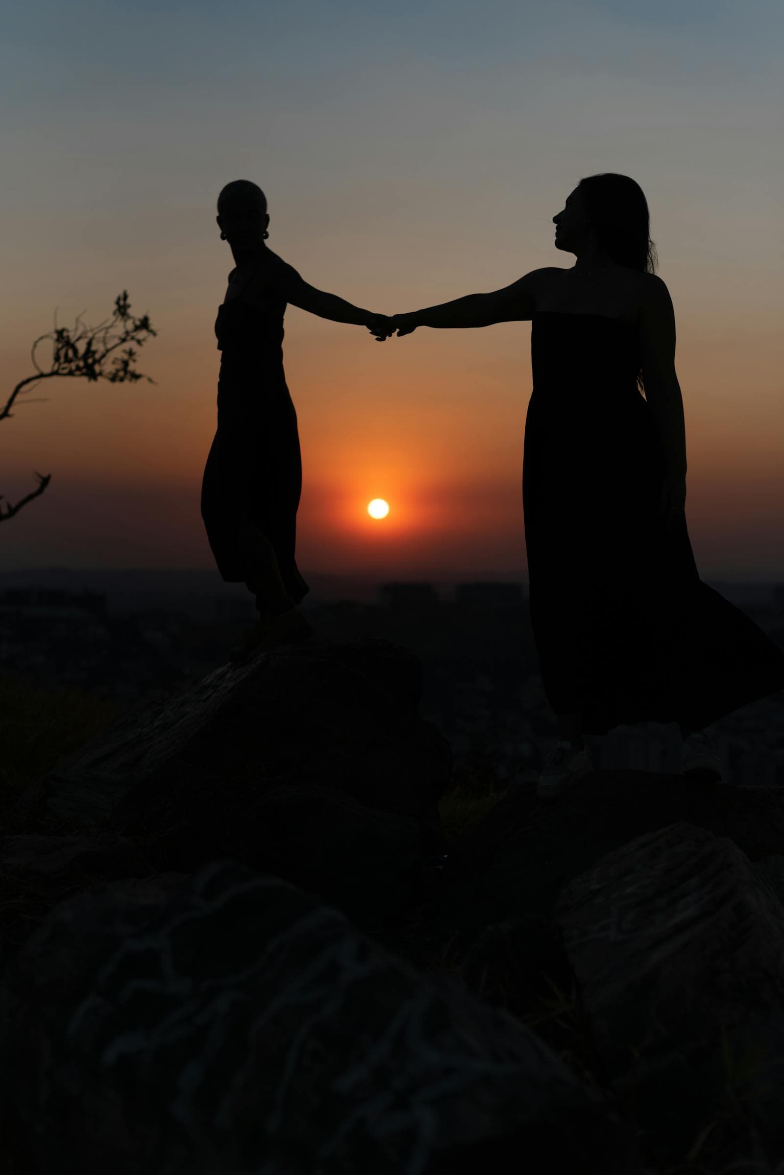 Silhouette of two women holding hands against a vibrant orange sunset sky