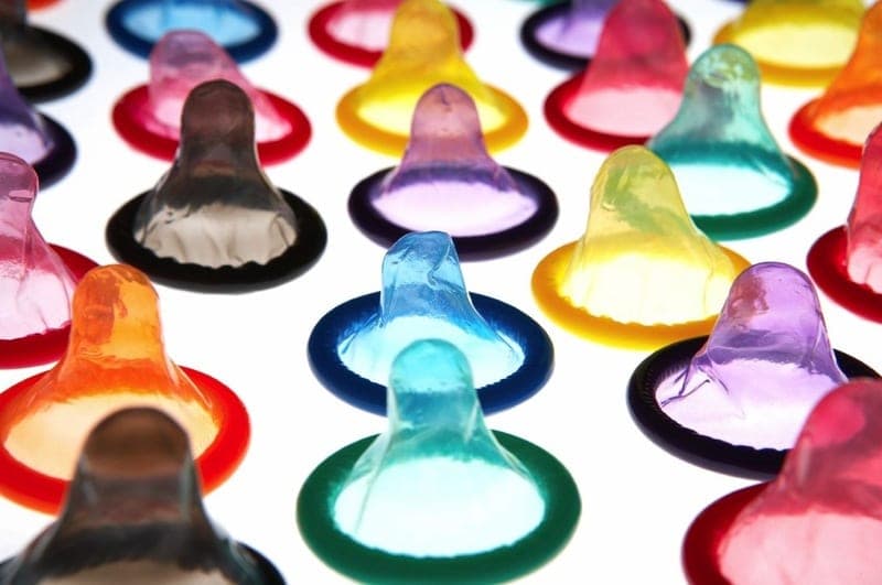 Rows of unrolled condoms in assorted translucent colors arranged on a white surface, photographed from a low angle
