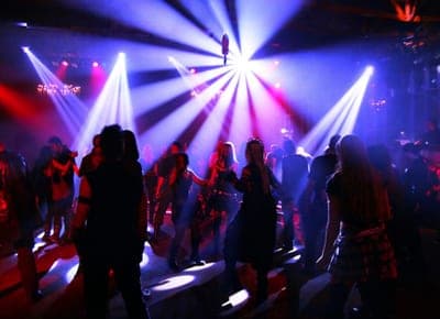Crowded nightclub dance floor silhouetted against bright blue and pink stage spotlights beaming from above