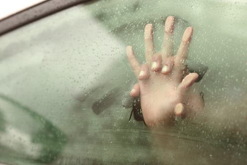 Close-up of a hand pressed against a rain-covered car window with condensation beading on the glass