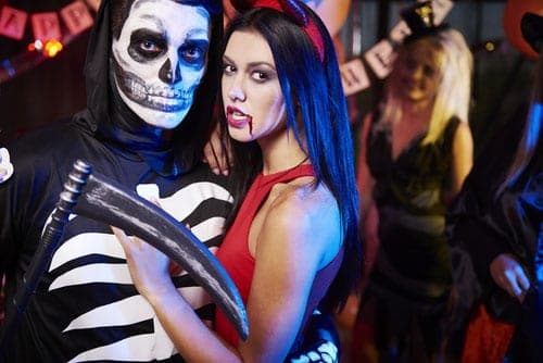 Couple in Halloween costumes, man as skeleton grim reaper and woman as red devil, at a party