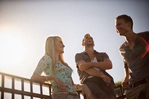 Woman and two men laughing together outdoors against a bright sunset backlight