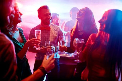 Group of friends laughing and clinking champagne flutes in a nightclub with pink and purple lighting