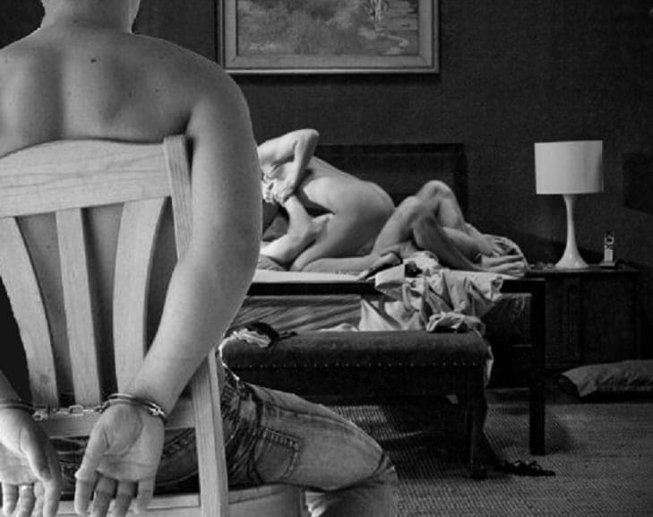 Black and white scene of a handcuffed person on a chair watching a couple embrace on a bed